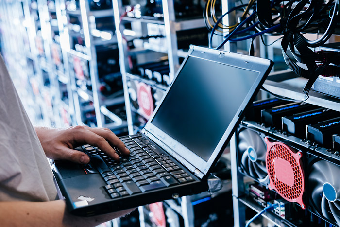 Ein Mitarbeiter steht vor einem Serverschrank und tippt auf seinem Laptop